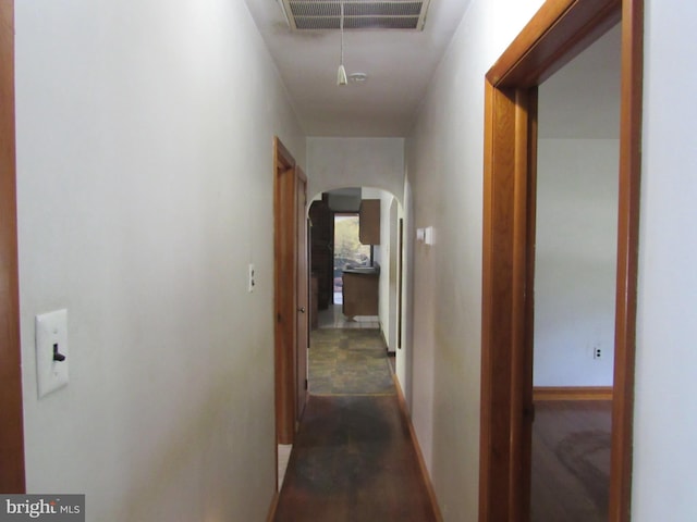 hall featuring visible vents, arched walkways, baseboards, and wood finished floors