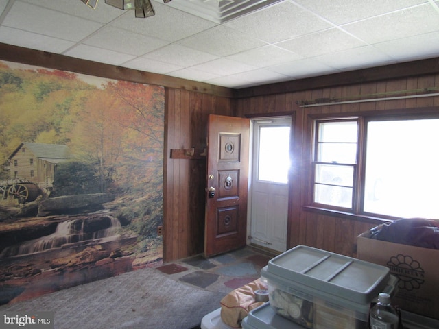 foyer entrance with wood walls and a paneled ceiling