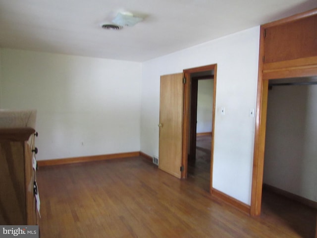 unfurnished bedroom with baseboards, wood finished floors, and visible vents