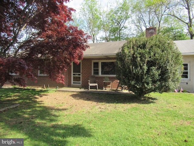 back of property featuring a lawn, a chimney, a shingled roof, and brick siding