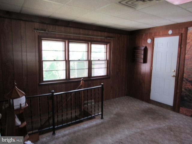 carpeted entrance foyer with visible vents, a paneled ceiling, and wooden walls