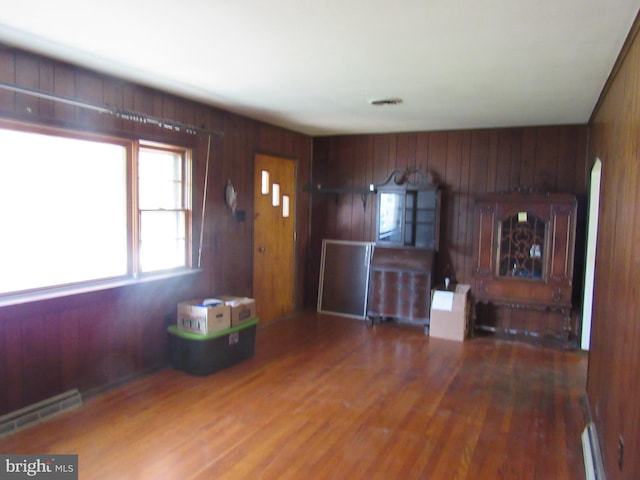 foyer entrance featuring baseboard heating, wood walls, wood finished floors, and visible vents