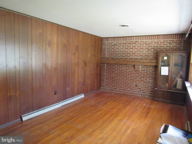 unfurnished room featuring a baseboard radiator, wooden walls, wood finished floors, and brick wall