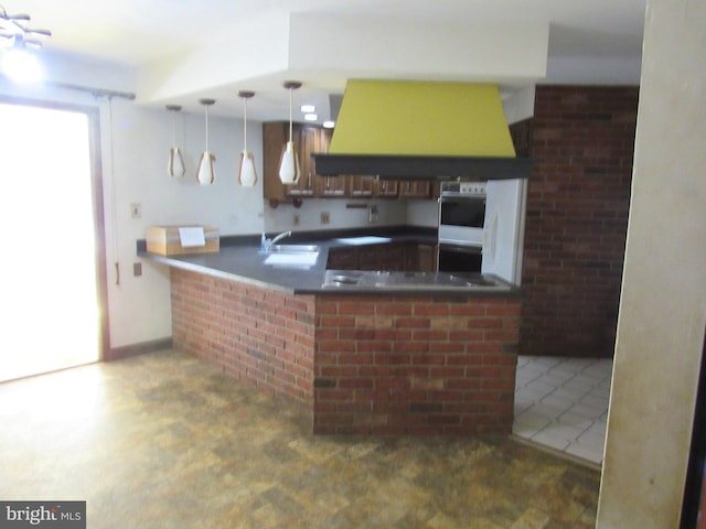 kitchen featuring pendant lighting, a peninsula, dark countertops, extractor fan, and a sink