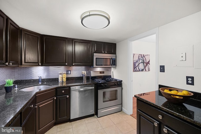 kitchen with a sink, stainless steel appliances, light tile patterned flooring, dark stone countertops, and tasteful backsplash