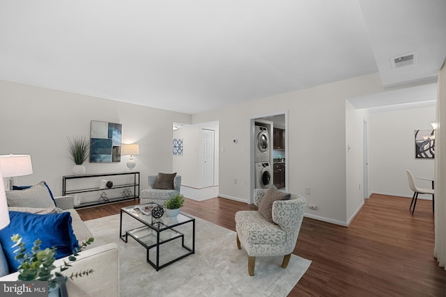 living area featuring stacked washer / drying machine, visible vents, wood finished floors, and baseboards
