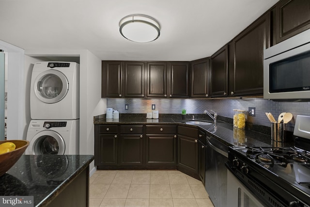 kitchen featuring stacked washer and dryer, light tile patterned floors, a sink, appliances with stainless steel finishes, and backsplash