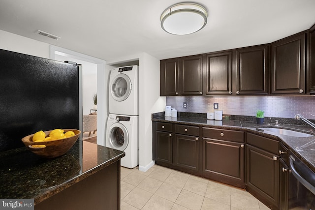 washroom with stacked washing maching and dryer, laundry area, light tile patterned floors, a sink, and visible vents