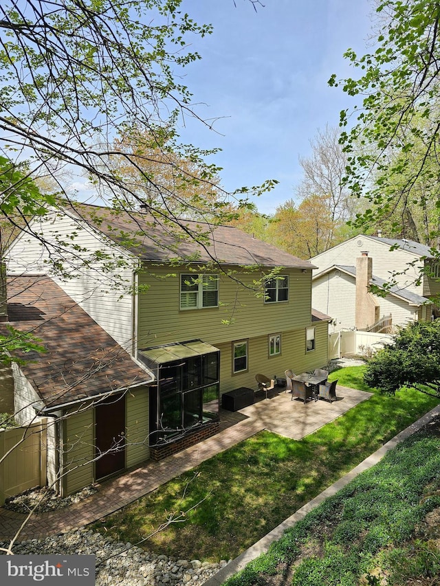 back of house with a sunroom, a patio area, a lawn, roof with shingles, and fence