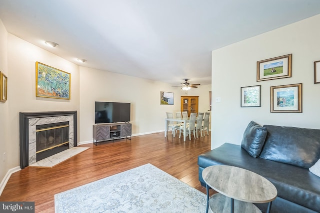 living room with a high end fireplace, ceiling fan, wood finished floors, and baseboards