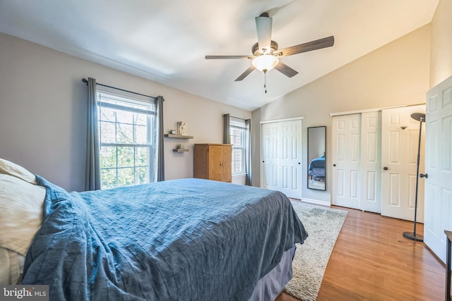 bedroom with multiple closets, wood finished floors, ceiling fan, and lofted ceiling