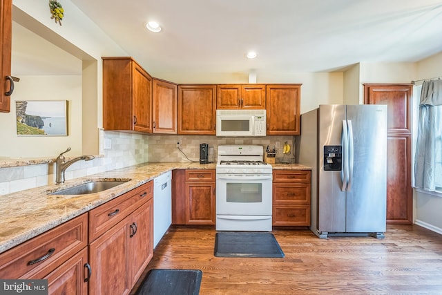kitchen with brown cabinets, a sink, light stone counters, and white appliances