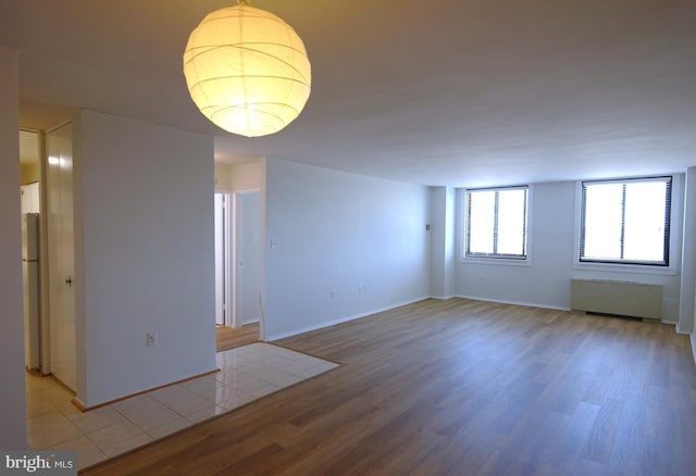unfurnished room featuring radiator, light wood finished floors, and baseboards