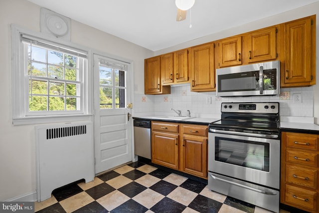 kitchen with stainless steel appliances, radiator heating unit, tile patterned floors, backsplash, and a sink