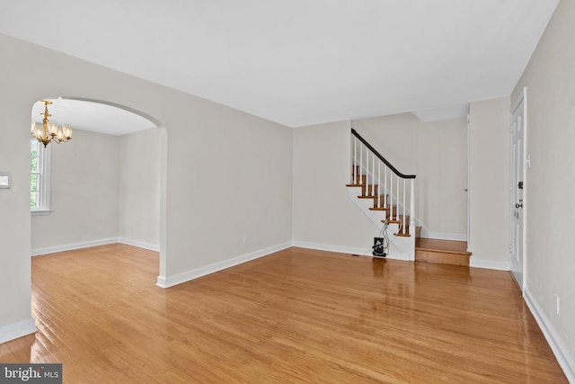 foyer entrance with light wood finished floors, arched walkways, a chandelier, stairs, and baseboards