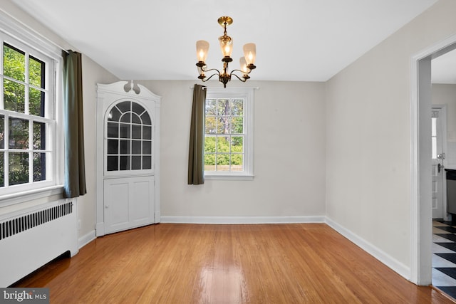 unfurnished dining area with radiator, a chandelier, wood finished floors, and baseboards