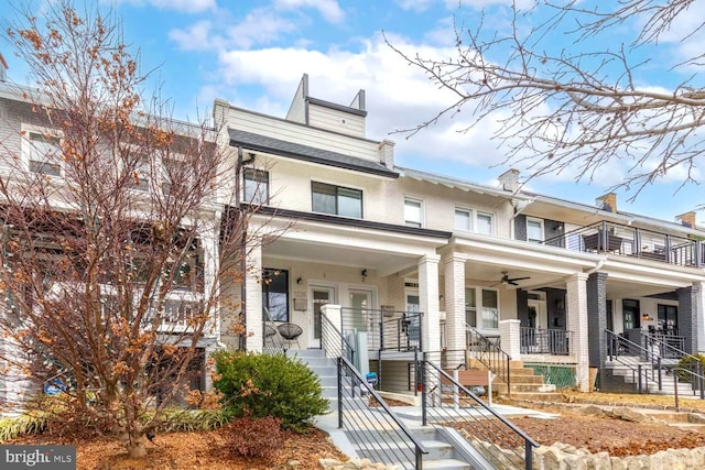 townhome / multi-family property with a porch, stairs, a chimney, and brick siding