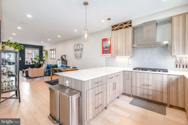 kitchen with stainless steel gas stovetop, light brown cabinets, a peninsula, and wall chimney exhaust hood