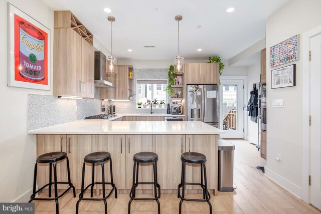 kitchen featuring stainless steel appliances, open shelves, wall chimney exhaust hood, light brown cabinetry, and a peninsula