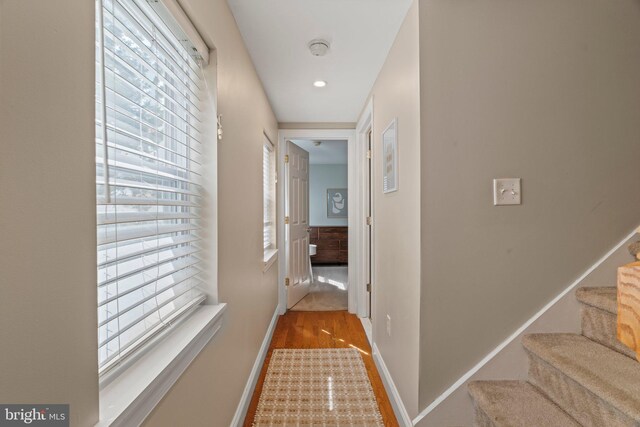 corridor featuring baseboards, wood finished floors, and stairs