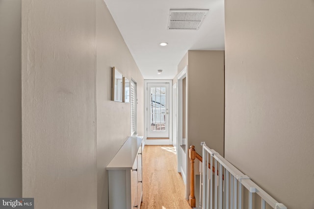 hallway with an upstairs landing, visible vents, and light wood-type flooring