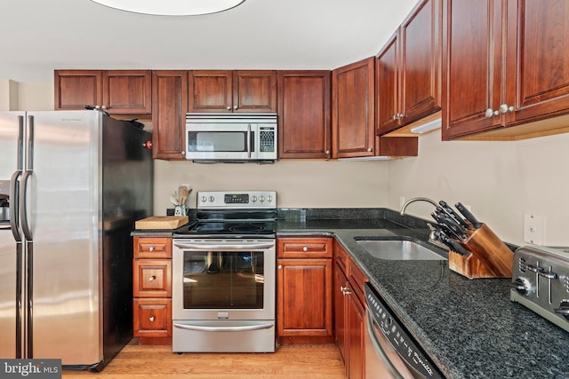 kitchen featuring dark stone counters, appliances with stainless steel finishes, light wood-style flooring, and a sink
