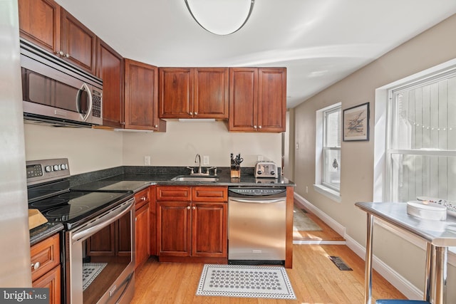 kitchen featuring dark stone counters, stainless steel appliances, light wood-type flooring, and a sink