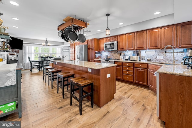 kitchen with appliances with stainless steel finishes, light stone countertops, brown cabinetry, and a sink