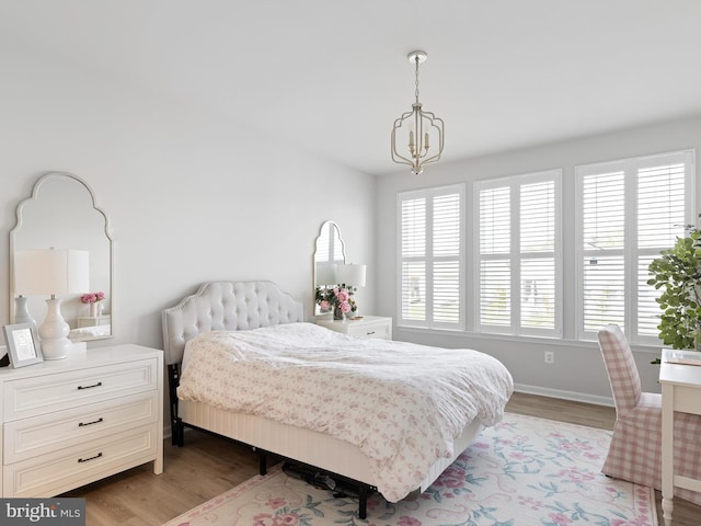 bedroom with baseboards, a notable chandelier, and light wood-style floors