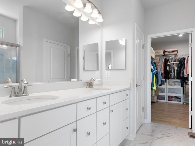 bathroom with double vanity, a spacious closet, marble finish floor, and a sink