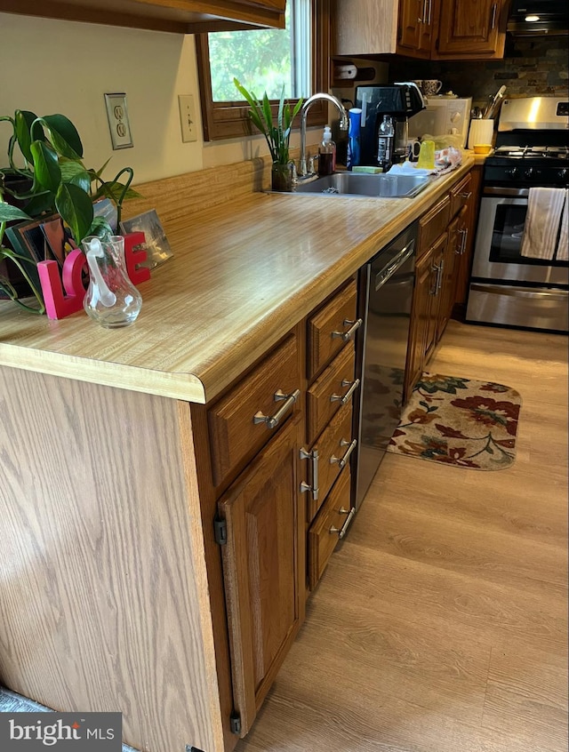 kitchen featuring a sink, gas range, wooden counters, light wood-type flooring, and dishwashing machine