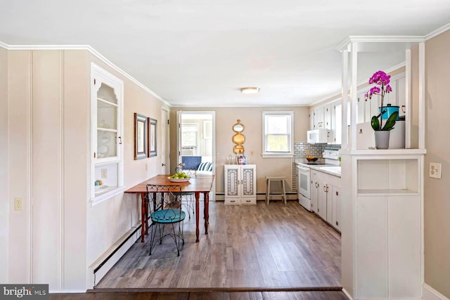kitchen with wood finished floors, white cabinets, a baseboard heating unit, ornamental molding, and white appliances