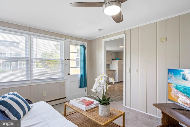 living area with ornamental molding, a ceiling fan, a decorative wall, and baseboard heating