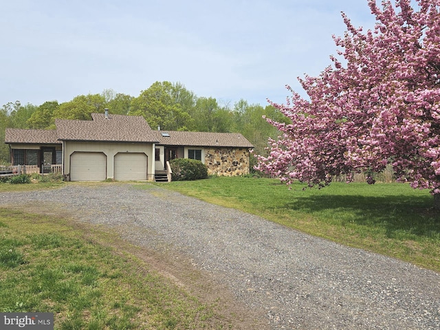 single story home with driveway, a front yard, an attached garage, and stone siding