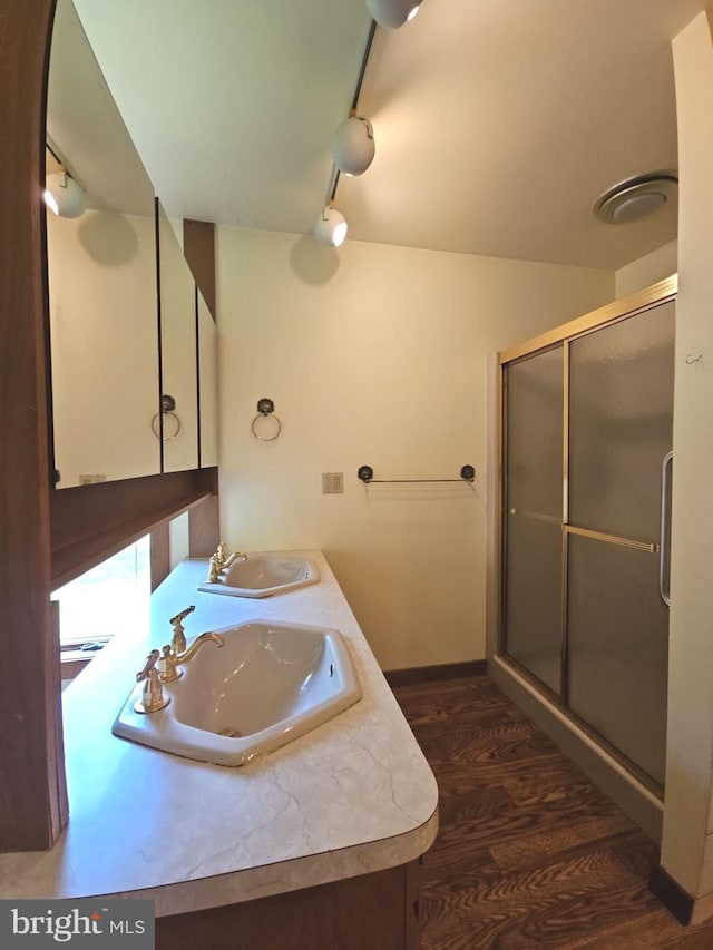 bathroom with track lighting, wood finished floors, a shower stall, and a sink
