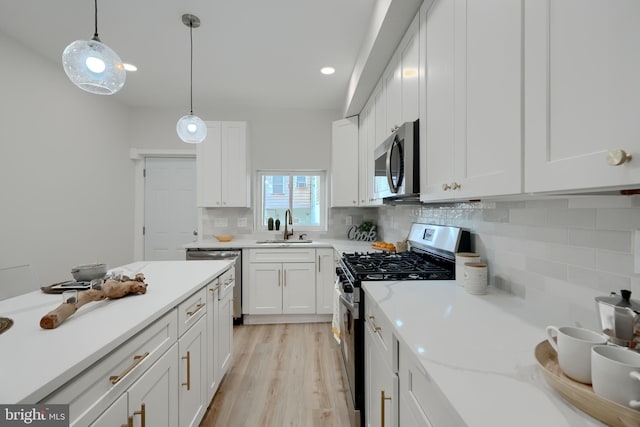 kitchen with hanging light fixtures, stainless steel appliances, white cabinets, backsplash, and a sink