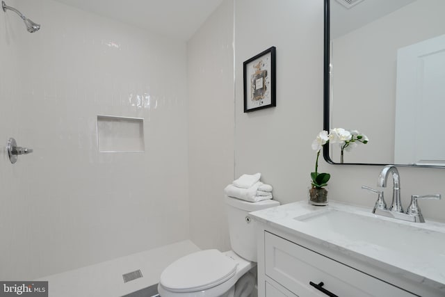 bathroom with tiled shower, toilet, and vanity