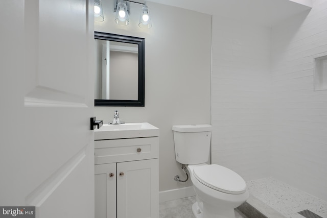 bathroom with tiled shower, vanity, toilet, visible vents, and baseboards
