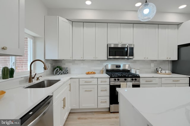 kitchen with light stone counters, stainless steel appliances, white cabinets, and a sink