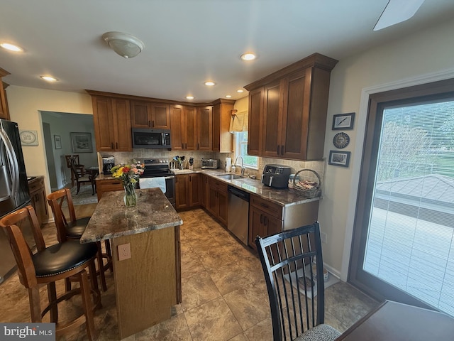 kitchen with dark stone counters, stainless steel appliances, backsplash, a sink, and a kitchen breakfast bar