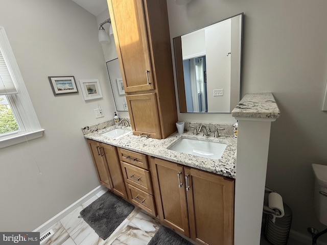 full bath with double vanity, baseboards, marble finish floor, and a sink