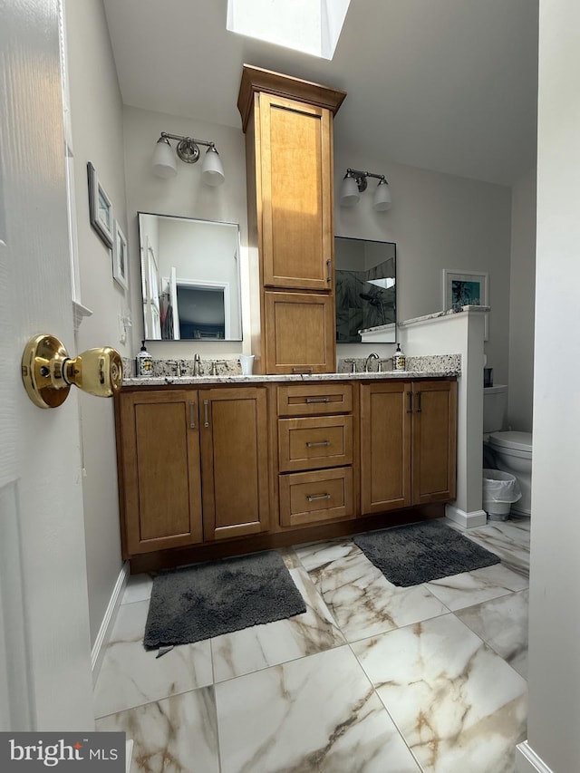 bathroom with toilet, a sink, marble finish floor, and double vanity