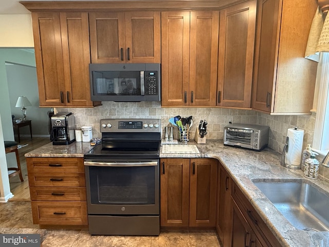 kitchen featuring brown cabinets, a sink, decorative backsplash, a toaster, and appliances with stainless steel finishes