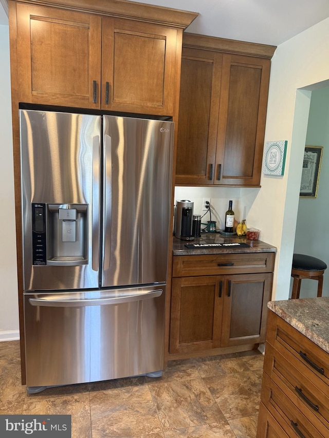 kitchen featuring stainless steel refrigerator with ice dispenser, brown cabinets, dark stone counters, and stone finish floor