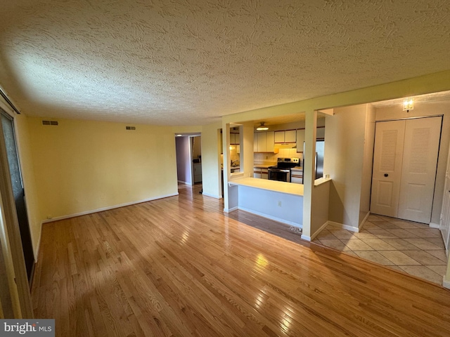 unfurnished living room featuring light wood-type flooring, a textured ceiling, baseboards, and visible vents