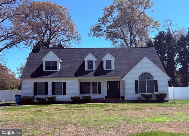 new england style home featuring a front lawn, roof with shingles, and fence