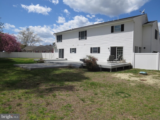 rear view of house featuring a deck, fence, and a lawn