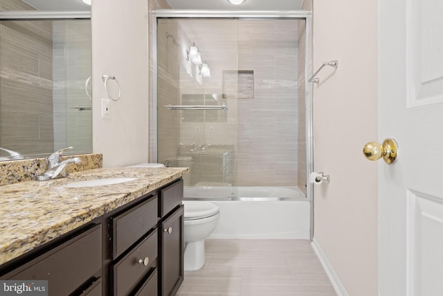 bathroom featuring toilet, combined bath / shower with glass door, vanity, and baseboards