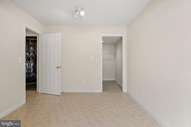 unfurnished bedroom with light tile patterned flooring, a closet, baseboards, and a walk in closet