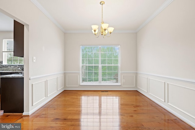 unfurnished dining area featuring ornamental molding, a wainscoted wall, a chandelier, and light wood-style floors